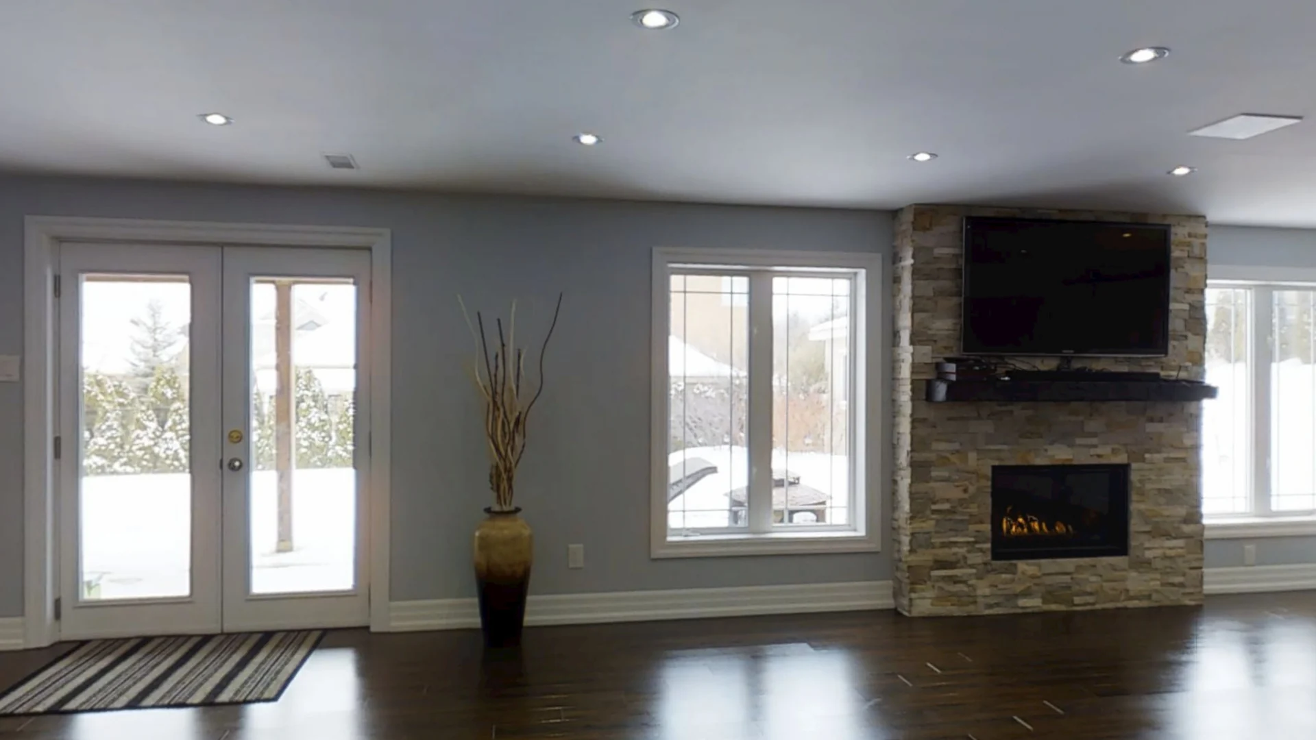 A finished walkout basement in Aurora: French doors to the yard, a tall window and the stacked-stone gas fireplace under the TV
