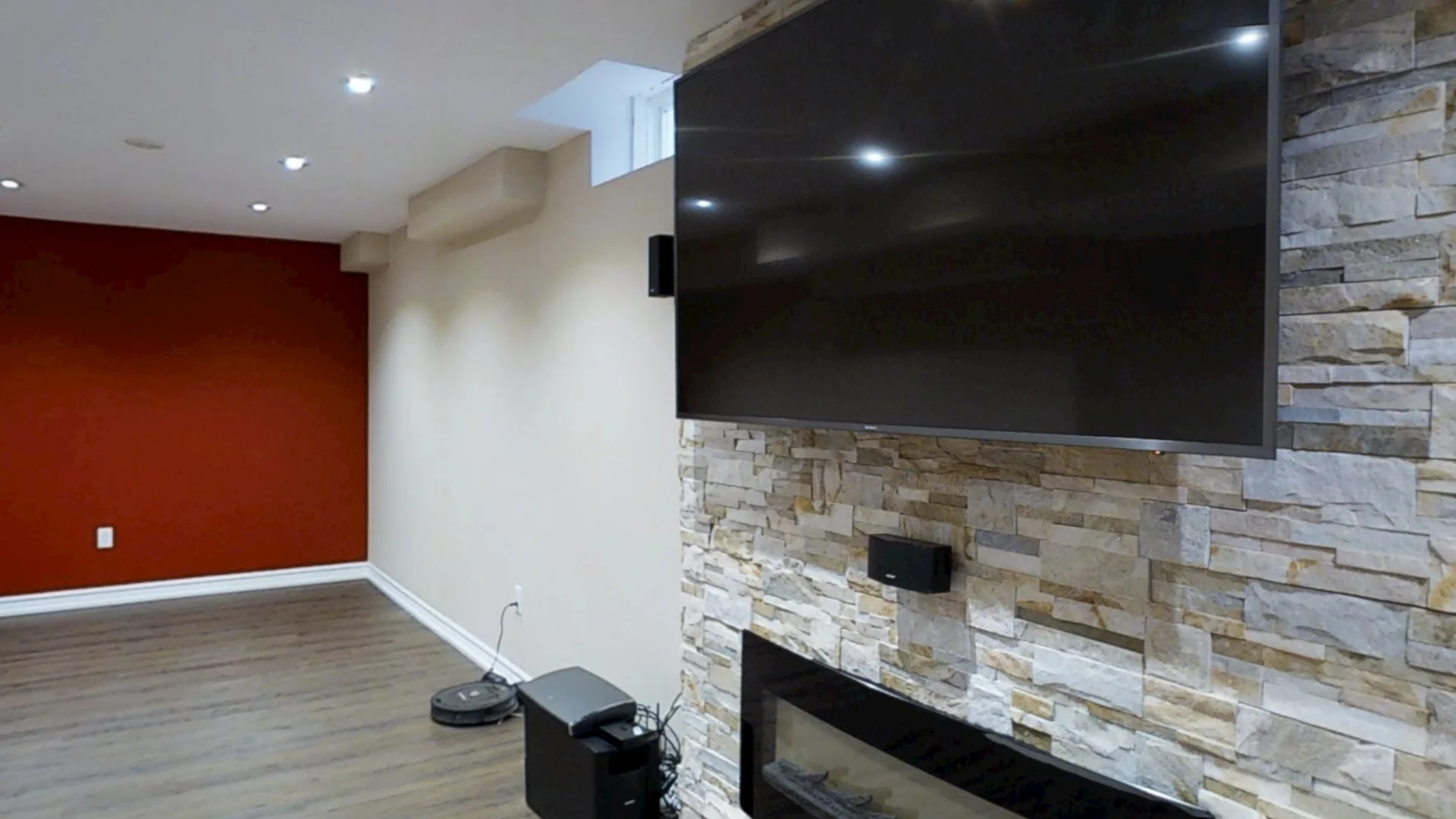 A finished Harmony basement: a stacked-stone wall with the TV above a linear electric fireplace, beside a red accent wall