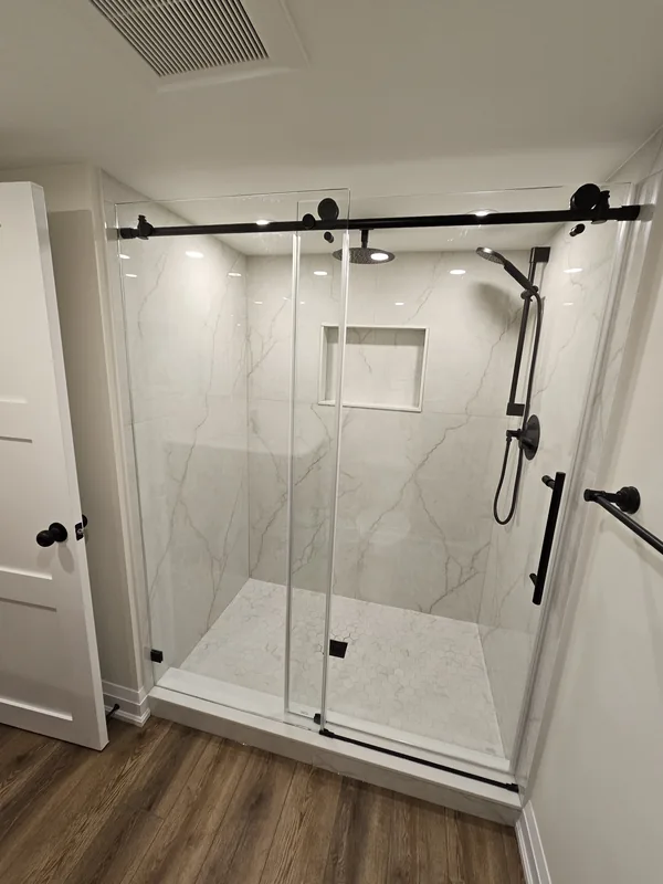 Basement bathroom renovation cost, Hamilton project: custom tiled shower with a sliding glass enclosure and a shampoo niche, by Harmony Basements