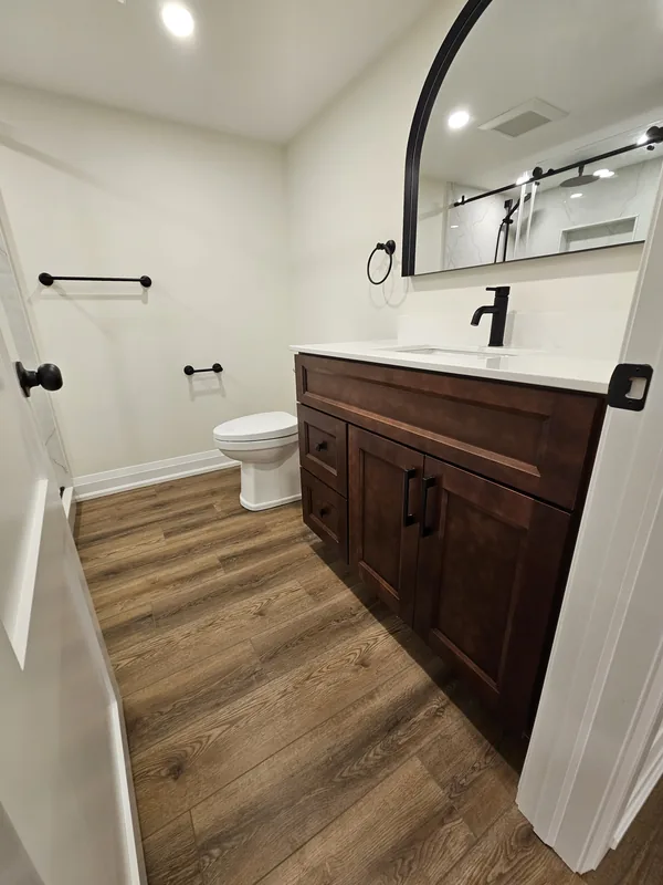 Finished basement bathroom Georgetown: the vanity with a black faucet and an arched mirror, by Harmony Basements — built in Hamilton