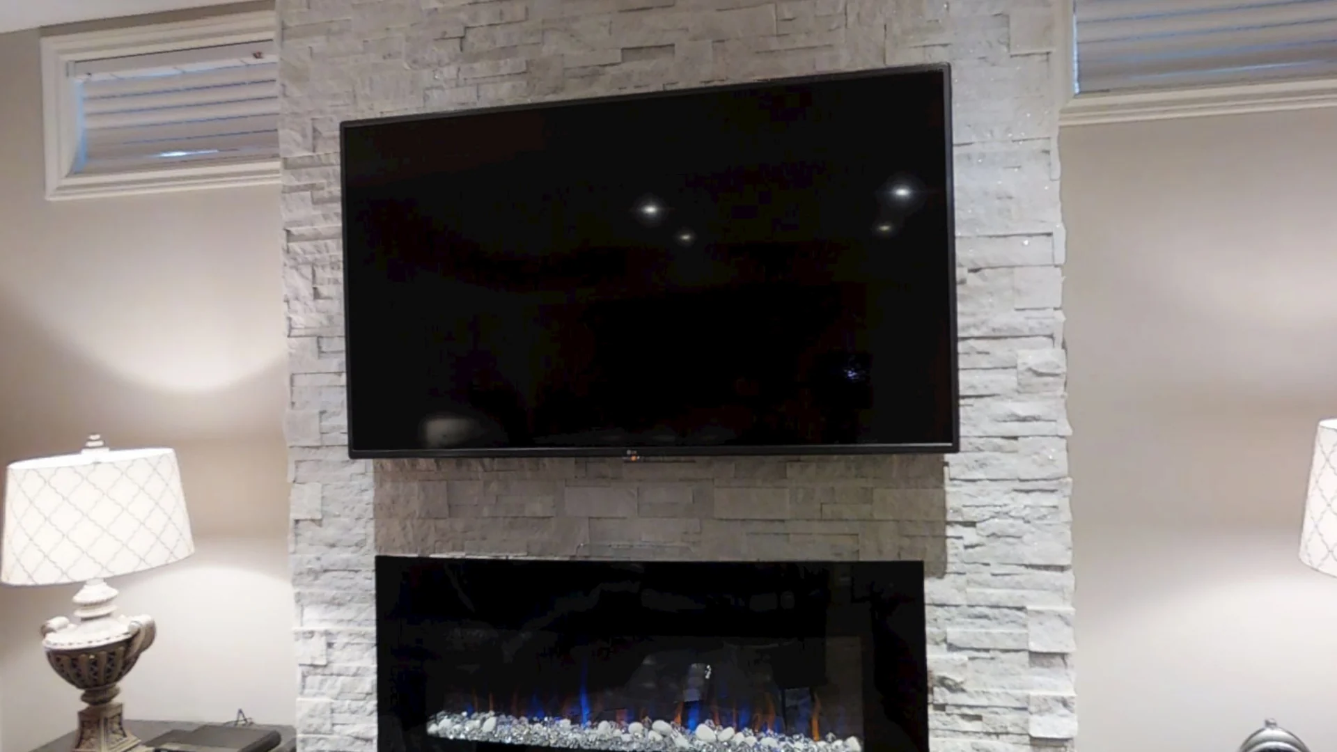 A finished basement in King City: a white stacked-stone wall with a linear electric fireplace, and the leather sectional