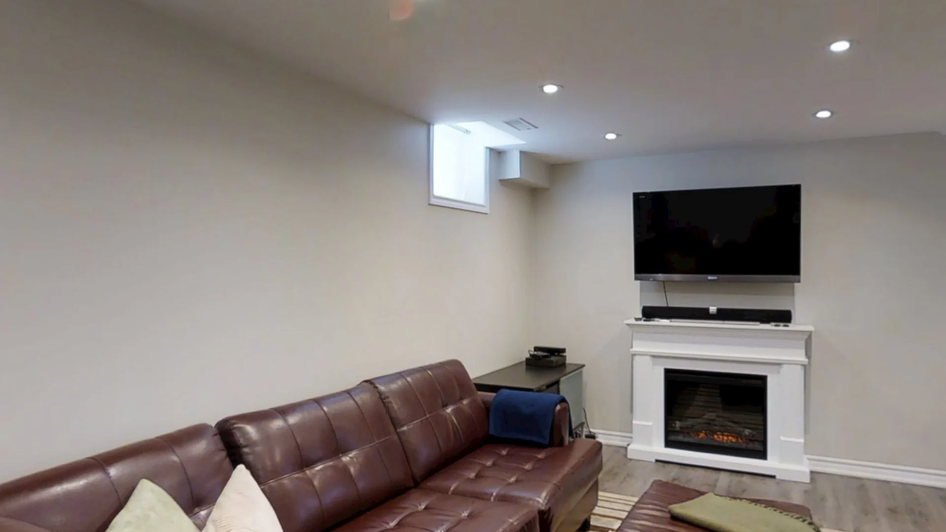 A finished Harmony basement: a leather sectional facing a white fireplace mantel with the TV above it