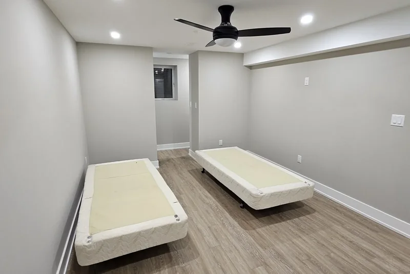 Finished basement bedroom cost, Vaughan project: grey painted walls and vinyl plank flooring, a black three-blade ceiling fan with a light, and a window set back in an alcove in the far wall.