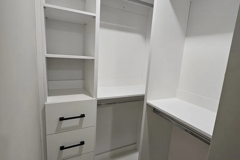 Basement finishing cost — Finished walk-in closet in a Vaughan basement: a white tower of open shelves above four drawers with black bar pulls, a double-hang bay with chrome rails beside it, and a return bay carrying a shelf over a rail, all on vinyl plank flooring.