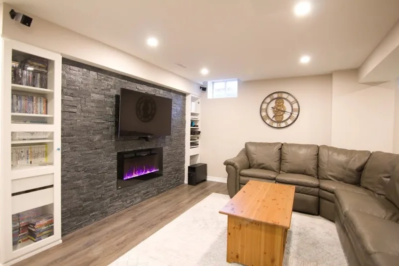A finished Harmony basement in Burlington: a stone media wall with a linear fireplace and built-in shelving, from the walkthrough film