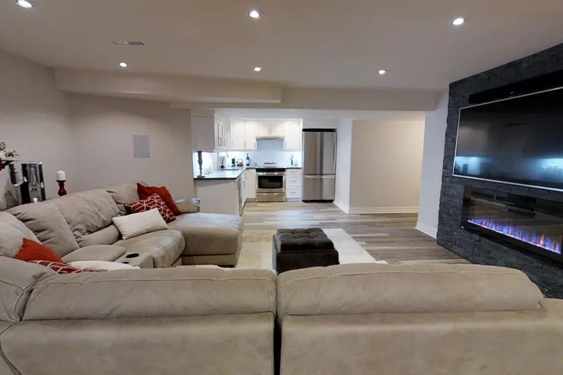 A finished Harmony basement: a large sectional, a media wall with a fireplace and the kitchen beyond, in the 3D tour