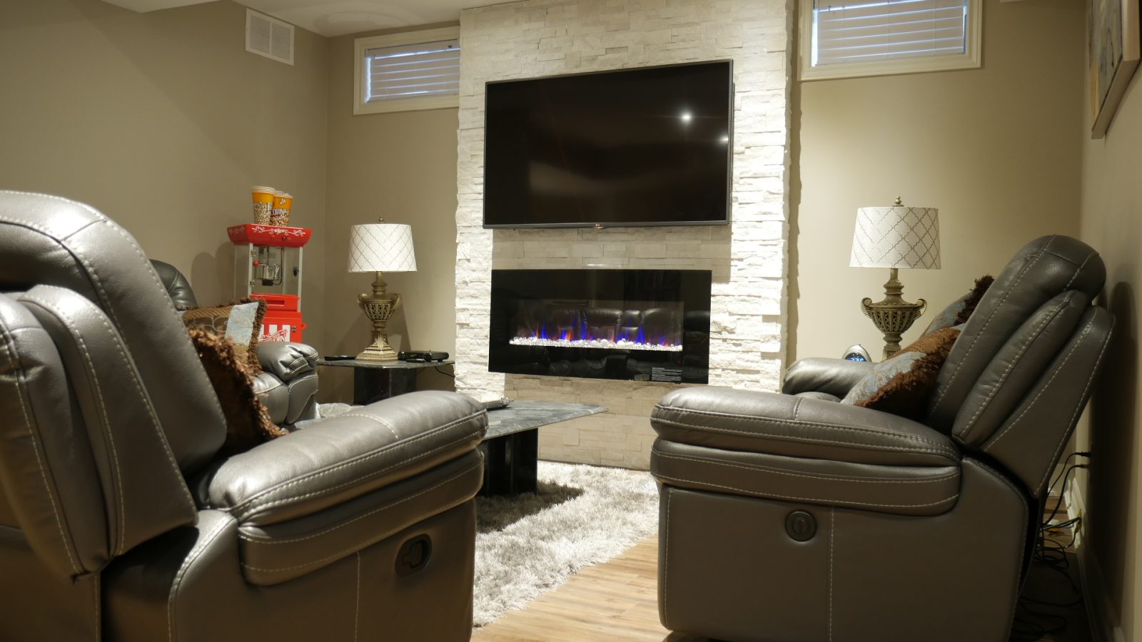 The family room: a white stacked-stone wall with a linear electric fireplace in a finished basement in King City by Harmony Basements