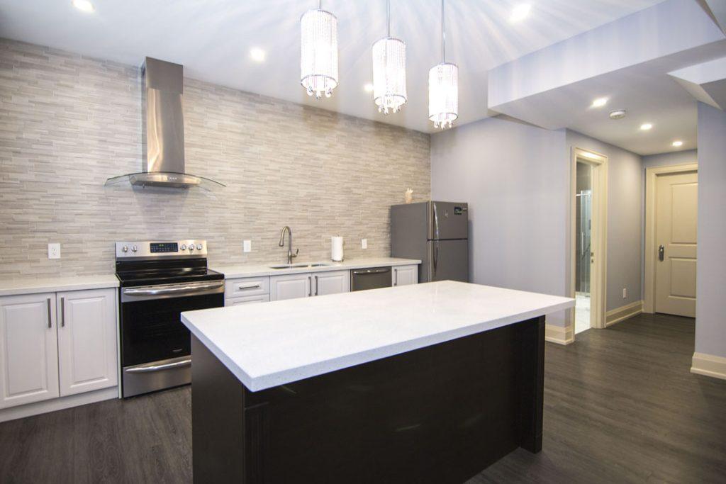 Basement kitchen with a white island, a range hood and pendant lights