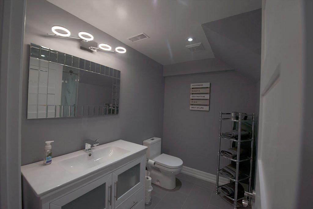 Grey basement bathroom with ring lights over the mirror and a white vanity