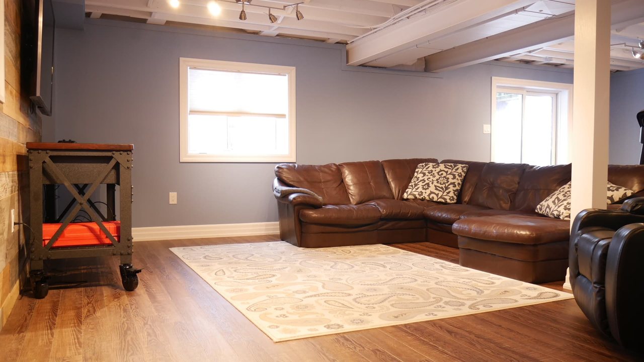 Basement family room in Bradford: a spray-painted exposed ceiling over luxury vinyl floors, by Harmony Basements