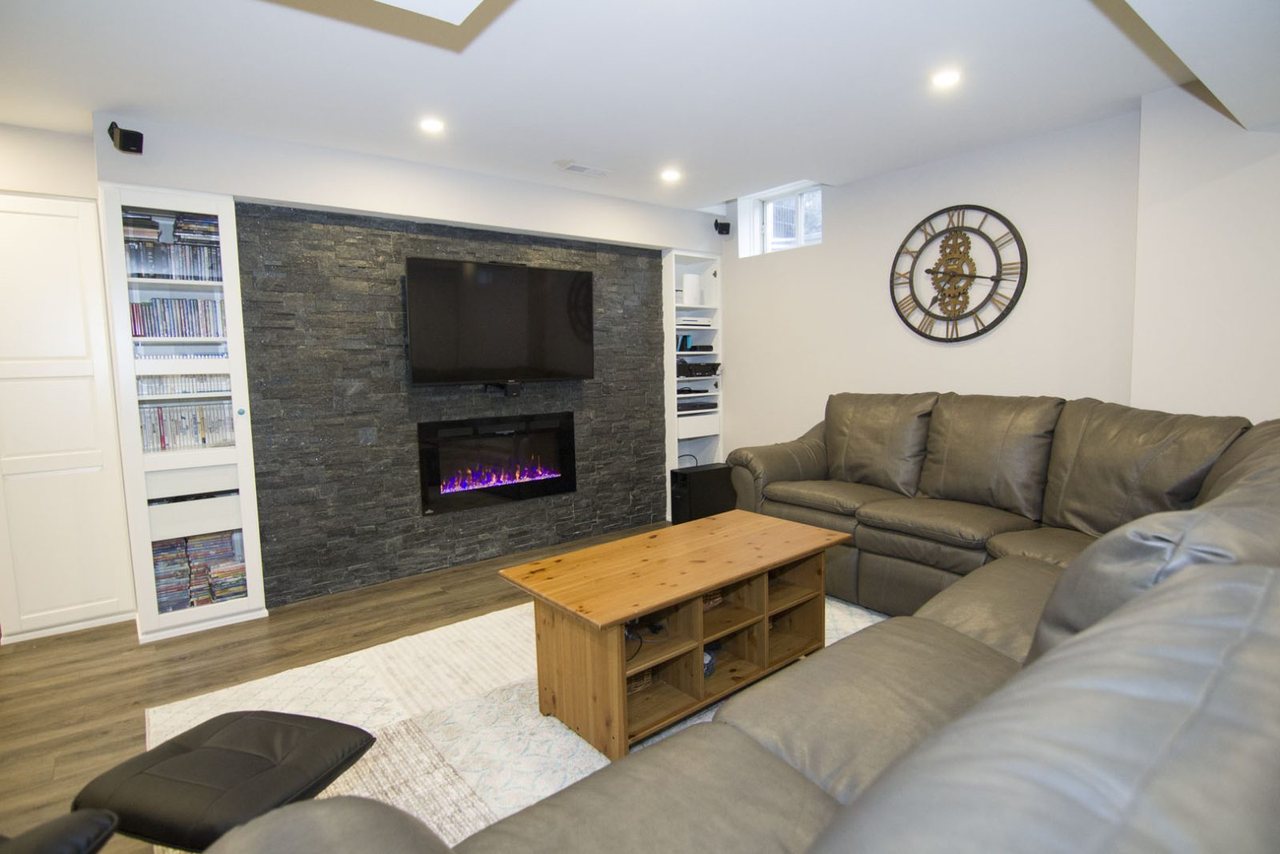 Basement fireplace in Burlington: a stacked-stone fireplace wall between built-in shelves, by Harmony Basements