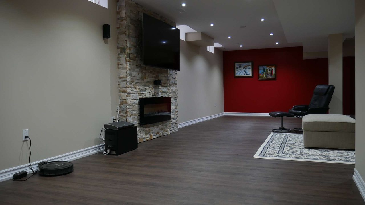 Basement fireplace in Milton: a TV above a linear electric fireplace on a natural stone wall &mdash; a finished basement by Harmony Basements