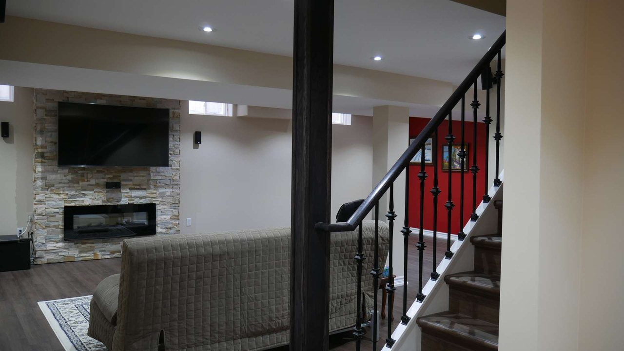 Basement open staircase in Milton: a railing, pickets and a post beside the stone wall &mdash; a finished basement by Harmony Basements